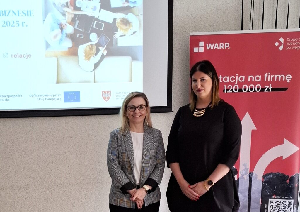 Na zdjęciu znajduje się Magdalena Franciszczak, dyrektorka projektu razem z Martą Juszczak, kierowniczką zespołu w WARP Sp. z o.o. podczas spotkania Nowej Energii w Biznesie w Kole. Obie prelegentki stoją na tle ekranu z prezentacją oraz roll-upu. 