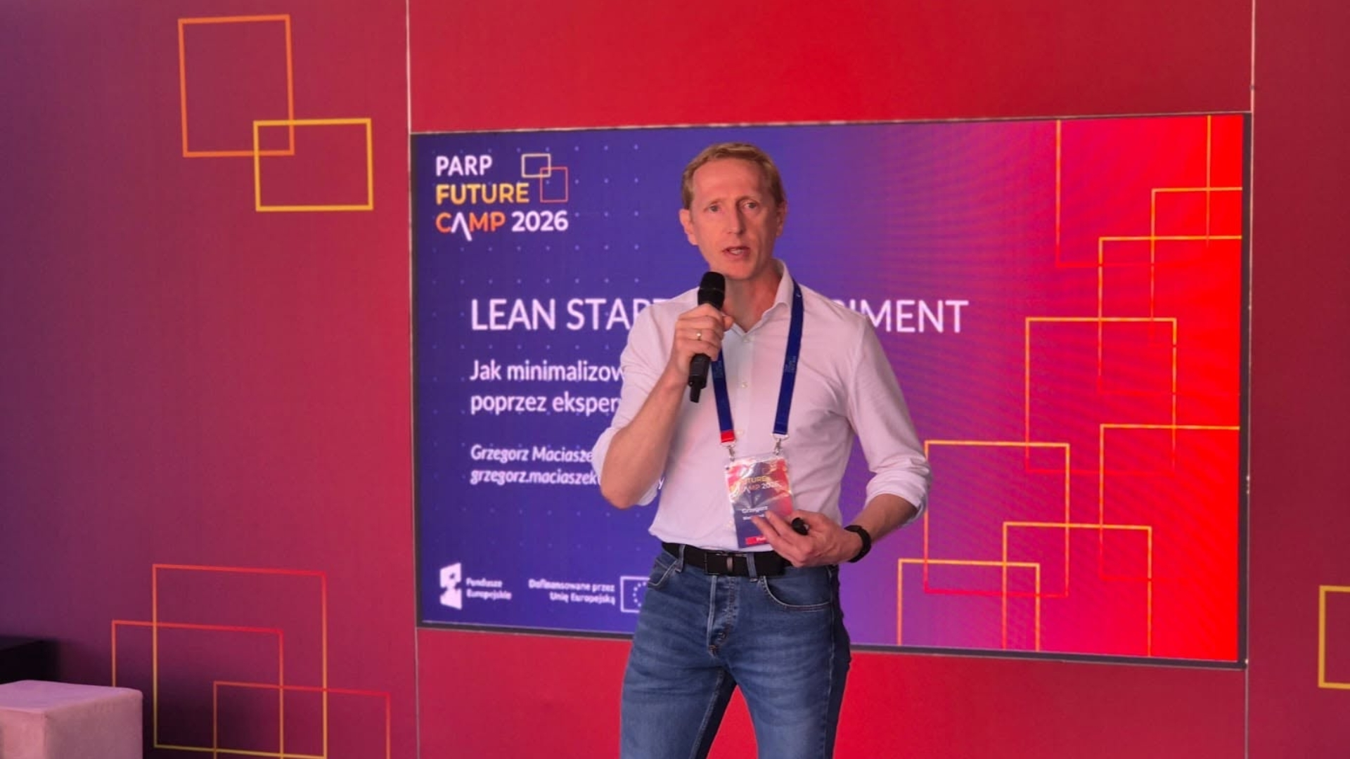 Grzegorz Maciaszek na scenie z mikrofonem podczas swojego warsztatu na PARP Future Camp 2026.