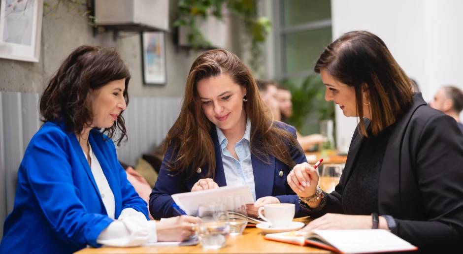 Zespół trzech pracowniczek DGA naradza się przy stole z dokumentami.